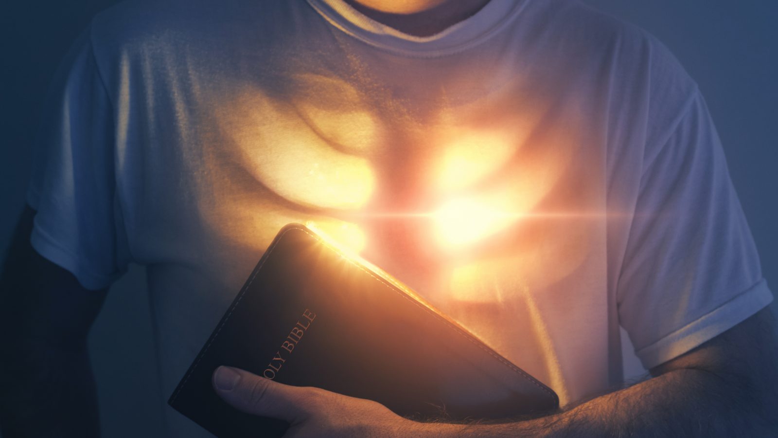 A man holds a Bible as his heart is glowing with bright lights